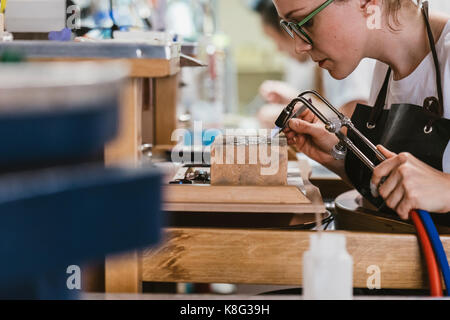 Weibliche Juwelier mit Brenner an der Werkbank Stockfoto