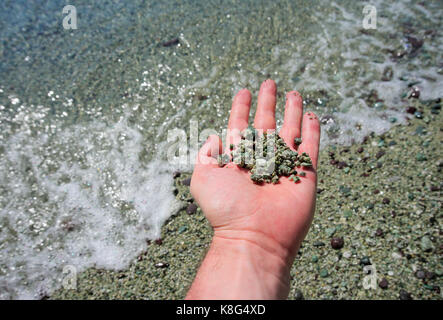 Hand mit Kieseln und Sand am Ufer des Meeres Stockfoto