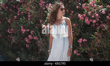 Frau in Sonnenbrille weg schauen beim Stehen gegen blühende Pflanzen Stockfoto