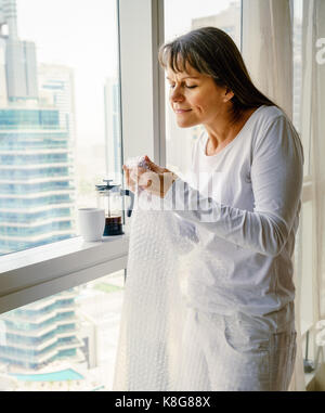 Reife Frau am Fenster ist Loslassen Stress durch knallende Luftpolsterfolie Stockfoto