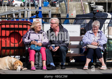 Padstow - Urlauber auf einem Aufenthalturlaub entspannen sich auf einer Bank am Hafen in Padstow an der Küste von Nord-Cornwall. Stockfoto