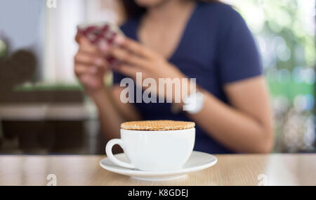 Nahaufnahme stroopwaffle auf heißen Kaffee Tasse und Unschärfe Frau warten Essen und mit Mobile auf Berufung Tag chatten Stockfoto