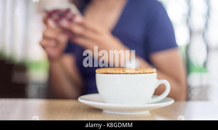 Nahaufnahme stroopwaffle auf heißen Kaffee Tasse und Unschärfe Frau warten Essen und mit Mobile auf Berufung Tag chatten Stockfoto