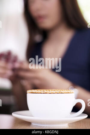 Nahaufnahme stroopwaffle auf heißen Kaffee Tasse und Unschärfe Frau warten Essen und mit Mobile auf Berufung Tag chatten Stockfoto