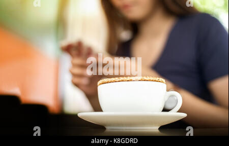 Nahaufnahme stroopwaffle auf heißen Kaffee Tasse und Unschärfe Frau warten Essen und mit Mobile auf Berufung Tag chatten Stockfoto