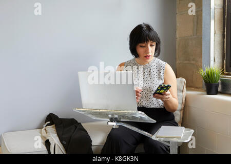 Frau sitzt mit Laptop auf Laptop Stand, Smartphone Stockfoto