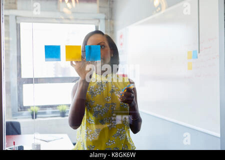 Junge Frau im Büro, selbstklebende Haftnotizen zu Glas im Büro Stockfoto
