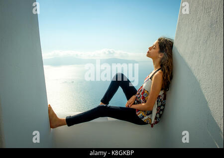 Mädchen sitzend, lehnte sich gegen die Wand, Meer im Hintergrund, Perissa, Santorini, Griechenland Kikladhes Stockfoto