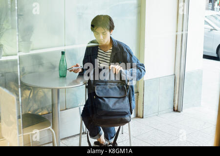 Junger Mann im Cafe sitzen, Sortieren durch Bag, Smartphone Stockfoto