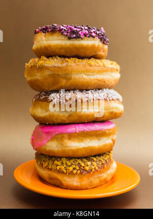 Stapel der sortierten Donuts auf eine orange Platte in einem weichen braunen Hintergrund Stockfoto