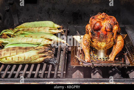 Eine voll geröstete Bier kann man Hähnchen auf dem Grill mit einem halben Dutzend gegrillte Maiskolben. Stockfoto