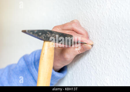 Hammer einen Nagel in eine weiße Wand in der Nähe von Stockfoto
