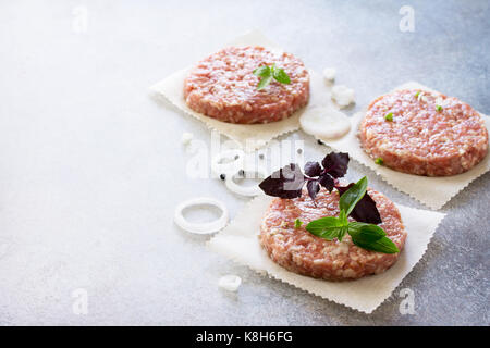 Raw-Hamburger-Schnitzel aus organischem Rindfleisch mit Gewürzen und Basilikum auf einem Stein oder Schiefer Hintergrund, Ansicht von oben mit der Kopie. Stockfoto