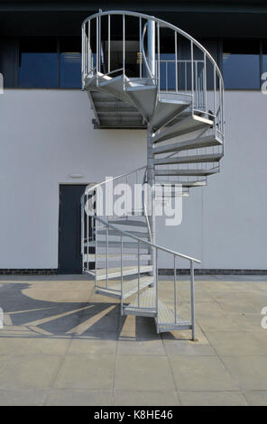 Eine Wendeltreppe aus verzinktem Stahl, die zu einem Parkplatz auf der Außenseite eines modernen Bürogebäudes. Stockfoto