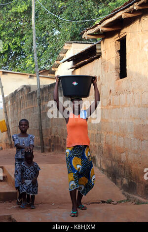 Afrikanisches Dorfleben. Wasserarbeit. afrikanisches Mädchen, das ein Becken mit Wasser auf dem Kopf trägt. togoville. togo. Stockfoto