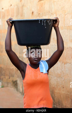 Afrikanisches Dorfleben. Wasserarbeit. afrikanisches Mädchen, das ein Becken mit Wasser auf dem Kopf trägt. togoville. togo. Stockfoto