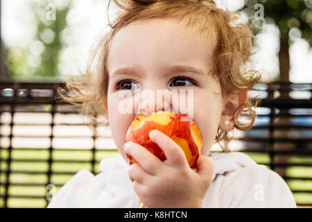 Süße Mädchen weg schauen, während Apple im Hof zu essen Stockfoto