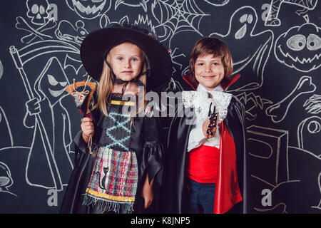 Kinder in Scary Hallowe'en Kostüme stehen gegen eine Wand mit Zeichnungen. Hexen und Dracula. Stockfoto
