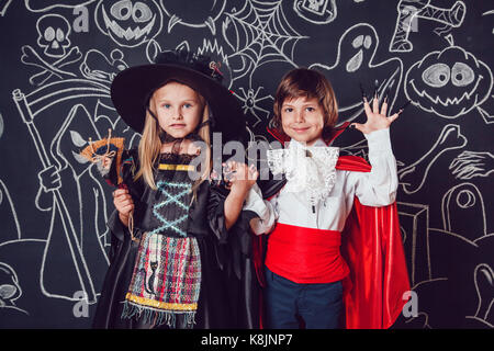 Kinder in Scary Hallowe'en Kostüme stehen gegen eine Wand mit Zeichnungen. Hexen und Dracula. Stockfoto