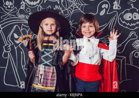 Kinder in Scary Hallowe'en Kostüme stehen gegen eine Wand mit Zeichnungen. Hexen und Dracula. Stockfoto