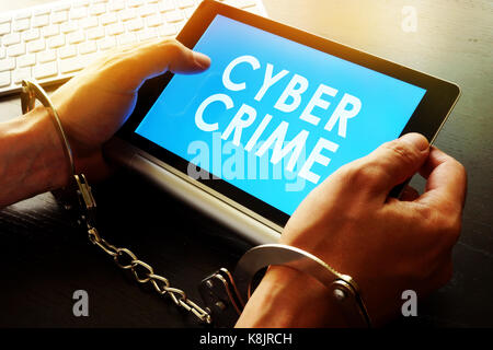 Mann in Handschellen holding Tablet mit Zeichen der Cyberkriminalität. Stockfoto