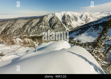 Schneeverwehungen auf dem Hang des Berges, auf den Sonnenuntergang mit Blick auf das Tal. Stockfoto