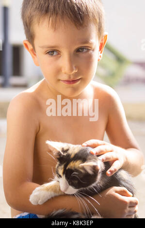 Süße kleine Jungen mit ein Kätzchen in der Hand posieren, Hintergrundbeleuchtung der Sonne Stockfoto