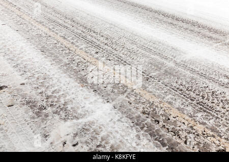 Kleine ländliche Straße mit Schnee bedeckt. Das Foto wurde in der Nähe getroffen. Auf der Fahrbahn Vision Schmutz Streifen auf den Autos, die Jahreszeit Winter. Stockfoto