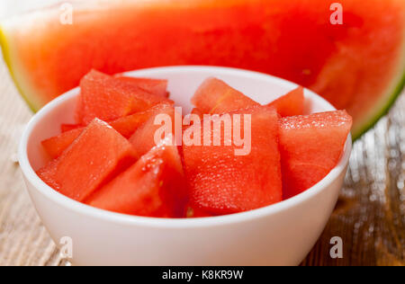 Rot, saftig und süß Wassermelone in Stücke schneiden und mit einer weißen Schüssel gefaltet. Im Hintergrund liegt ein ganzes Stück Wassermelone. schließen Foto oben Stockfoto