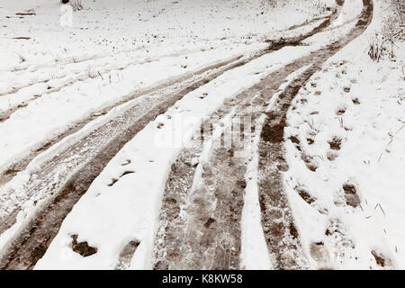 Titel von den Rädern der Autos auf einer Landstraße mit Schnee bedeckt unbefestigt. In den Schnee, Es gibt Spuren. Auf der Seite der Erhöhung der trockenen Gras Stockfoto