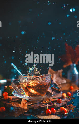 Aktion Herbst noch Leben mit Tee Tasse, Holzachterbahn, Herbst Blätter und Beeren, Tl und einen in Bewegung splash auf einem dunklen Hintergrund eingefroren. Stockfoto