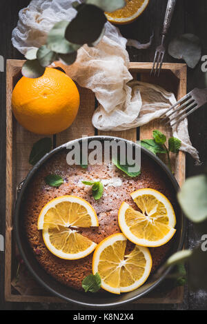 Orange Kuchen mit Orangenscheiben und minzeblatt auf Holz fach Ansicht von Oben eingerichtet. Essen still life Stockfoto