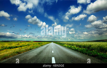 Bild der weiten Prärie mit eine asphaltierte Straße erstreckt, so weit das Auge sehen kann mit schönen kleinen grünen Hügeln unter strahlend blauem Himmel in t Stockfoto