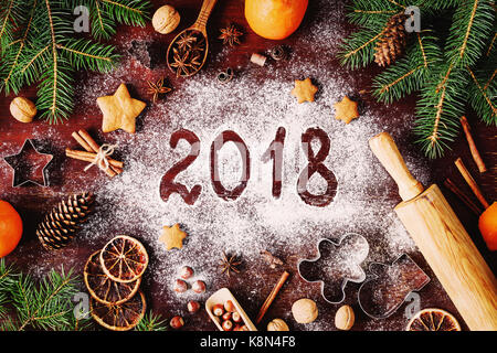 Frohes Neues Jahr 2018 Geschrieben von Mehl und Weihnachtsschmuck Lebkuchen cookies, Cinnamin, Orangen, Gewürzen, Nüssen und Ausstechformen auf hölzernen Hinterg Stockfoto