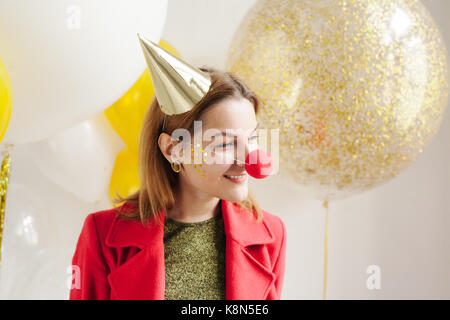 Junge Frau in einem feierlichen Kappe um Narren an einer Partei auf dem Hintergrund sinkender Konfetti Stockfoto