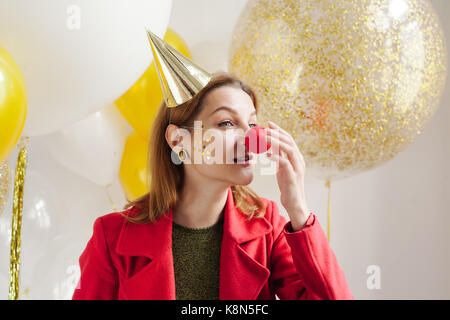 Junge Frau in einem feierlichen Kappe um Narren an einer Partei auf dem Hintergrund sinkender Konfetti Stockfoto