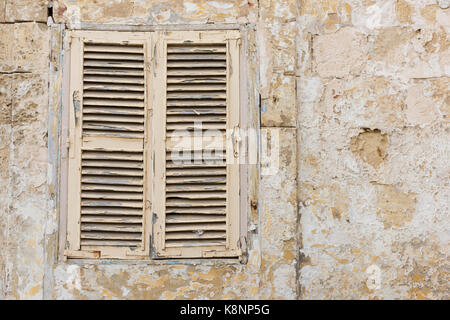 Ein altes Fenster mit Fensterläden auf einem Gebäude in Malta mit abblätternder Farbe und Textur Stockfoto