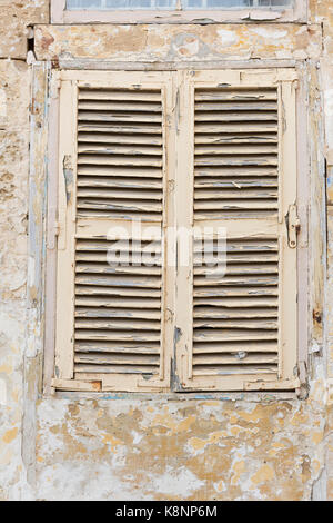 Ein altes Fenster mit Fensterläden auf einem Gebäude in Malta mit abblätternder Farbe und Textur Stockfoto