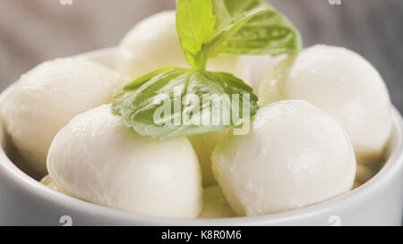 kleine Kugeln aus Mozzarella in Schüssel mit Basilikum Stockfoto