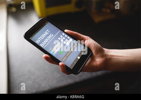 Internet banking Text auf Blau mobile Display gegen 7/8 Hand der Frau mit Telefon in der Küche Stockfoto