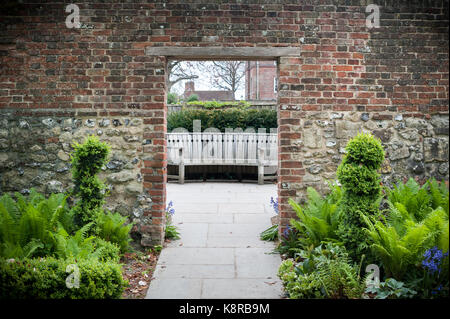 Einen Fußweg durch eine Mauer auf eine Holzbank im Bishops Palace Garden in Chichester, West Sussex, UK. Stockfoto