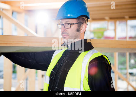 Tischler in Schutzkleidung tragen Holz auf der Schulter Stockfoto