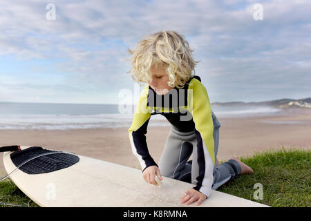 Junge Junge, bereit zum Surfen mit seinem Surfbrett am Strand das Tragen von Neoprenanzug an einem Sommertag. Stockfoto