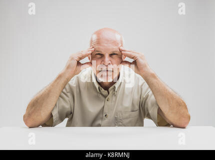 Nachdenklich, älterer Mann mit einer konzentrierten Ausdruck der Konzentration schielen, als er nachdenklich starrt in die Luft mit seinen Händen über seine Schläfen Stockfoto