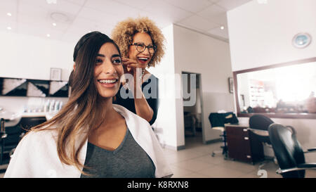 Weibliche Friseur arbeiten an Design, wie es eine Frau Haar. Friseur in einer glücklichen Stimmung während der Arbeit auf das Haar einer Frau Stil. Stockfoto