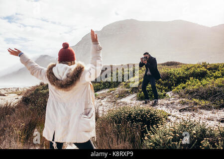 Junger Mann die Bilder seiner Freundin im Freien stehend mit erhobenen Armen. Paar am Strand Fotografieren mit der digitalen Kamera. Stockfoto