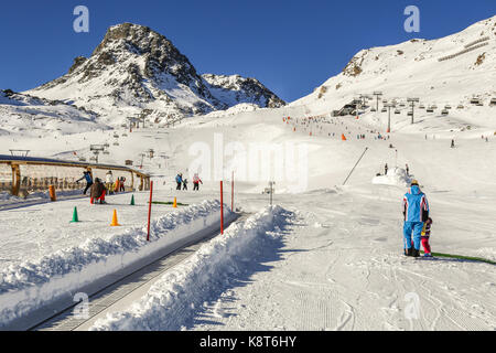 Winter Resort mit Ski Kinder in der Schule mit Zauberteppich Förderband, Kursleiter ans Skipisten zwischen Bergen im Hintergrund. Österreich, Ischg Stockfoto