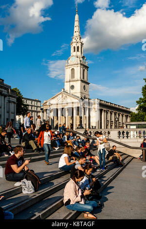 Junge Leute sitzen auf den Stufen des Trafalgar Square mit der Kirche von St. Martin-In-The-Fields im Hintergrund, London, UK Stockfoto