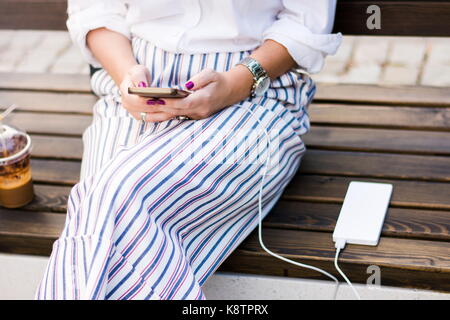 Mädchen mit Smart Phone während des Ladevorgangs auf dem Power Bank Stockfoto