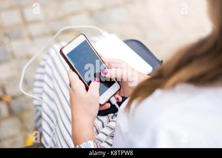 Mädchen mit Smart Phone während des Ladevorgangs auf dem Power Bank Stockfoto